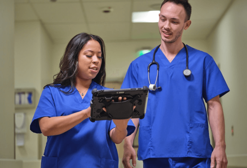 Two clinicians interact while looking at a tablet.