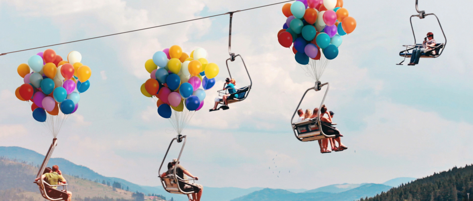 People on a ski lift that is carrying them up and powered by colorful balloons. 