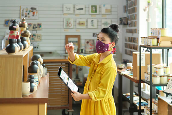 Retail worker wearing mask in pottery shop tracks inventory using a tablet and stylus