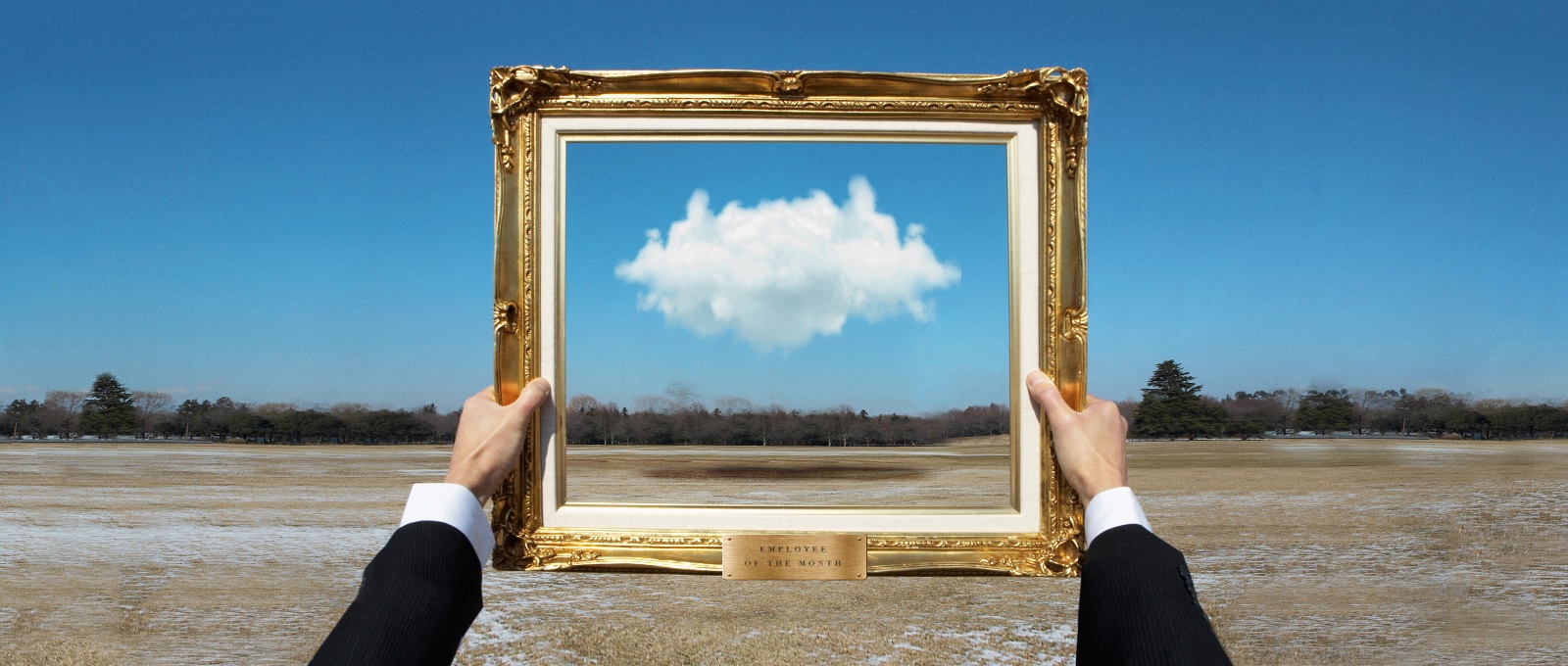A pair of hands holding a golden decorative frame to highlight a single cloud in the distance