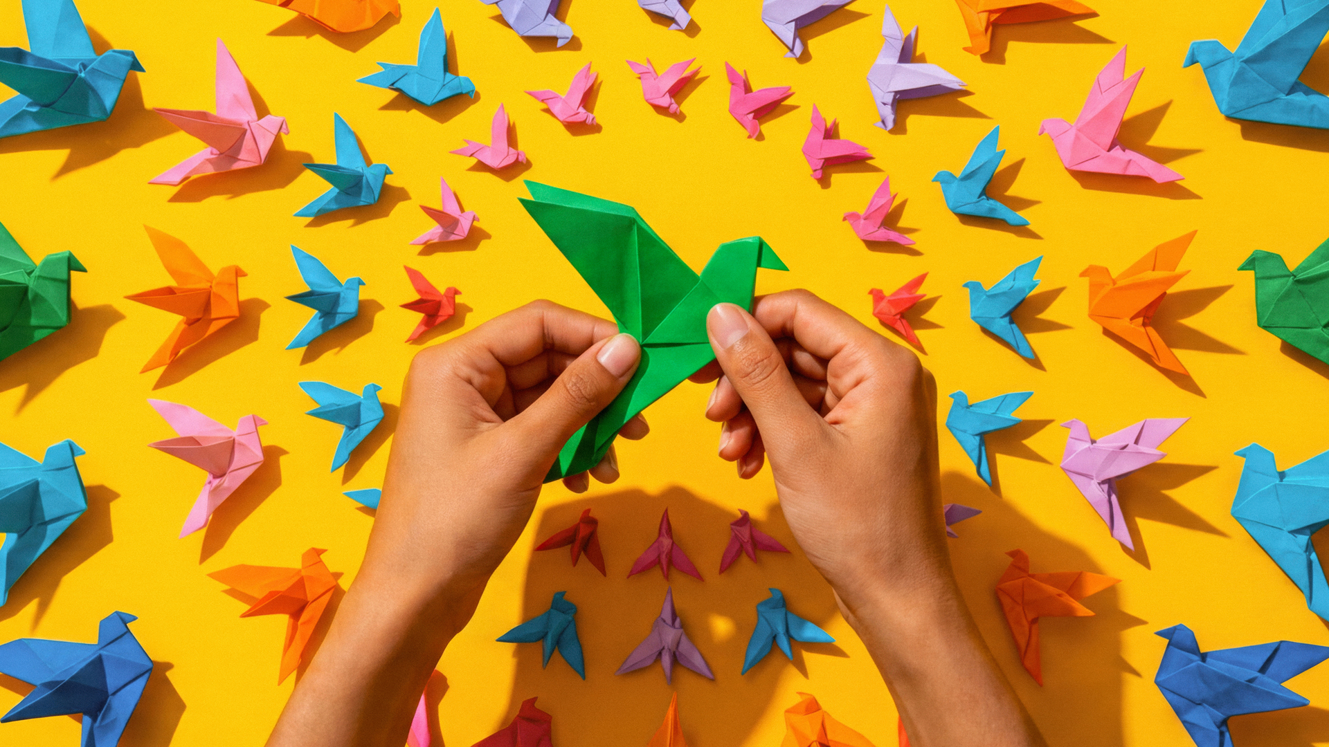 Hands folding origami shapes, representing the careful shaping of new organizational structures as work is redesigned around human judgment and AI. 